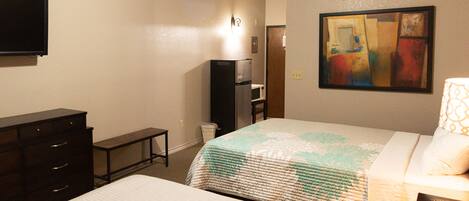 Habitación de hotel con dos camas, un aparador, un televisor, un refrigerador y un cuadro en la pared.