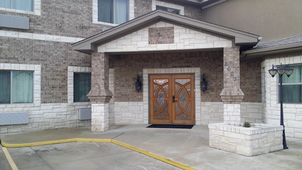 A building with a stone facade, a wooden double door with decorative glass panels, and a small entrance area with a yellow curb. - Premium Inn and Suites (Killeen)