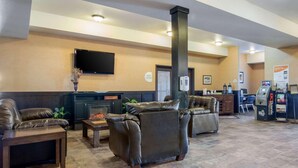 A lobby with leather sofas, a fireplace, a TV mounted on the wall, and a self-service kiosk.