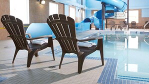 An indoor swimming pool with a blue slide, two Adirondack chairs, and a no running, no horseplay sign.