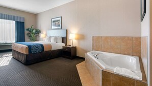A hotel room with a large bed, a separate bathroom with a bathtub, a nightstand with a lamp, and a window with curtains.
