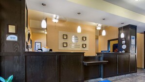 A hotel reception area with a wooden reception desk, a blue mat with the hotel logo, and framed pictures on the wall.