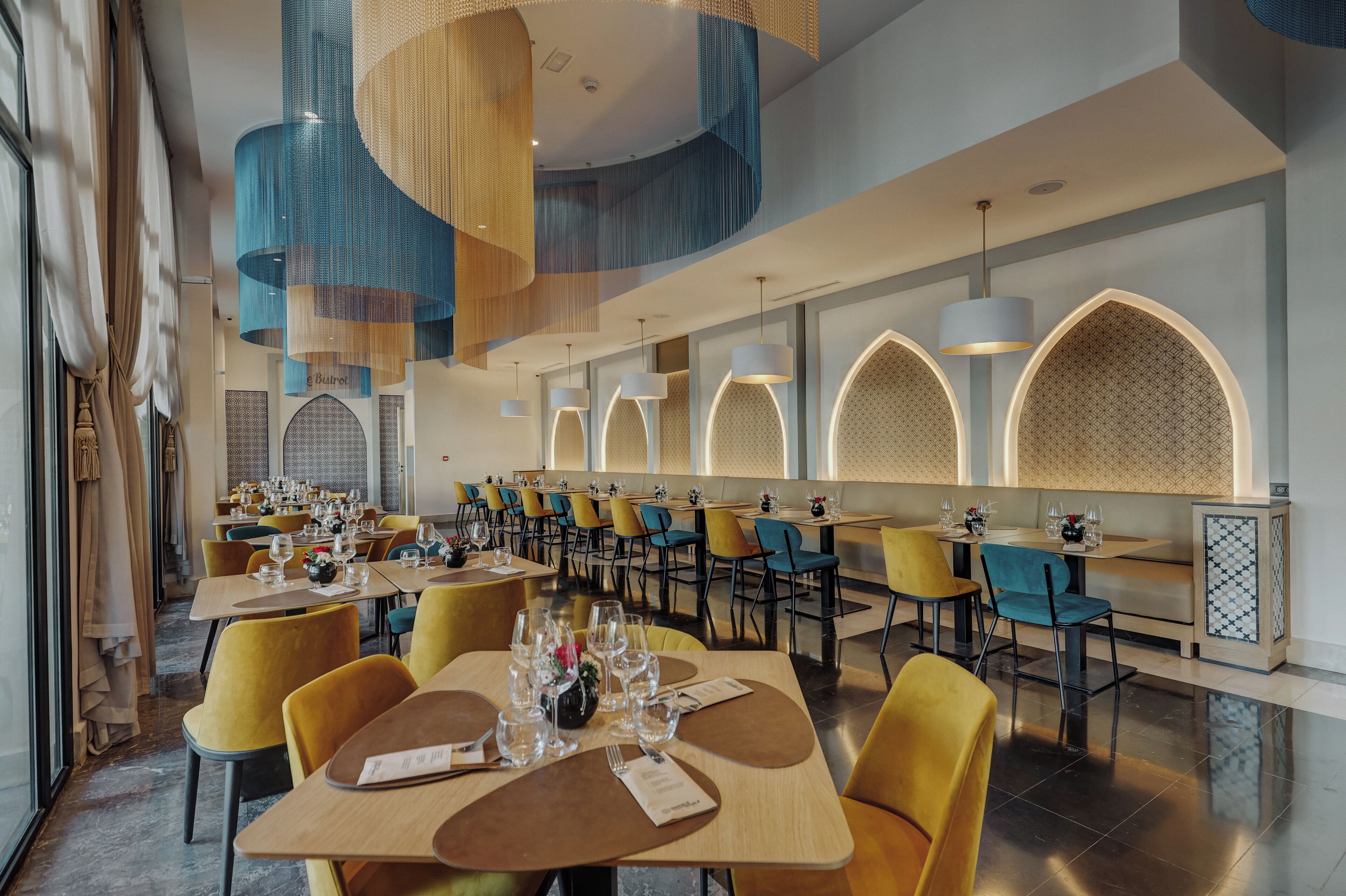 A modern dining area with yellow chairs, round tables, and blue hanging light fixtures.