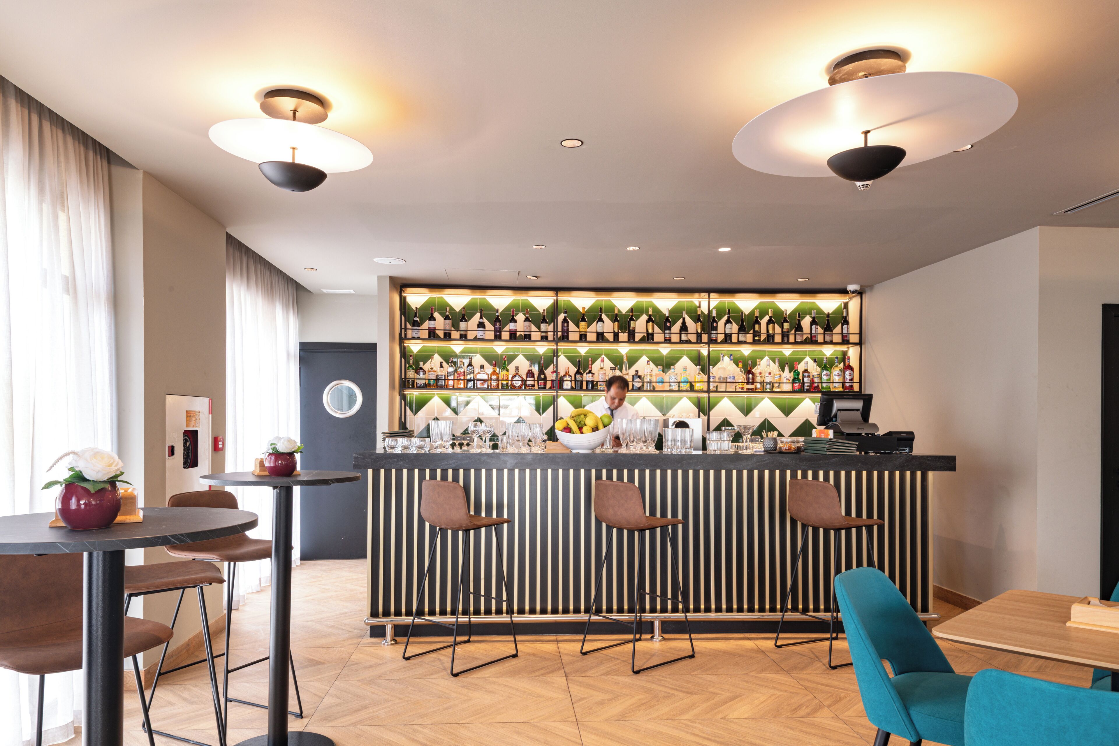 A modern bar area with a bartender, wooden bar counter, and striped wall decorations.