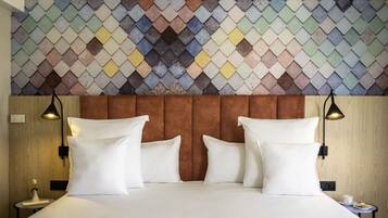 Quarto de hotel com cama, almofadas brancas, cabeceira, duas mesas de cabeceira e parede com design de azulejos estampados.