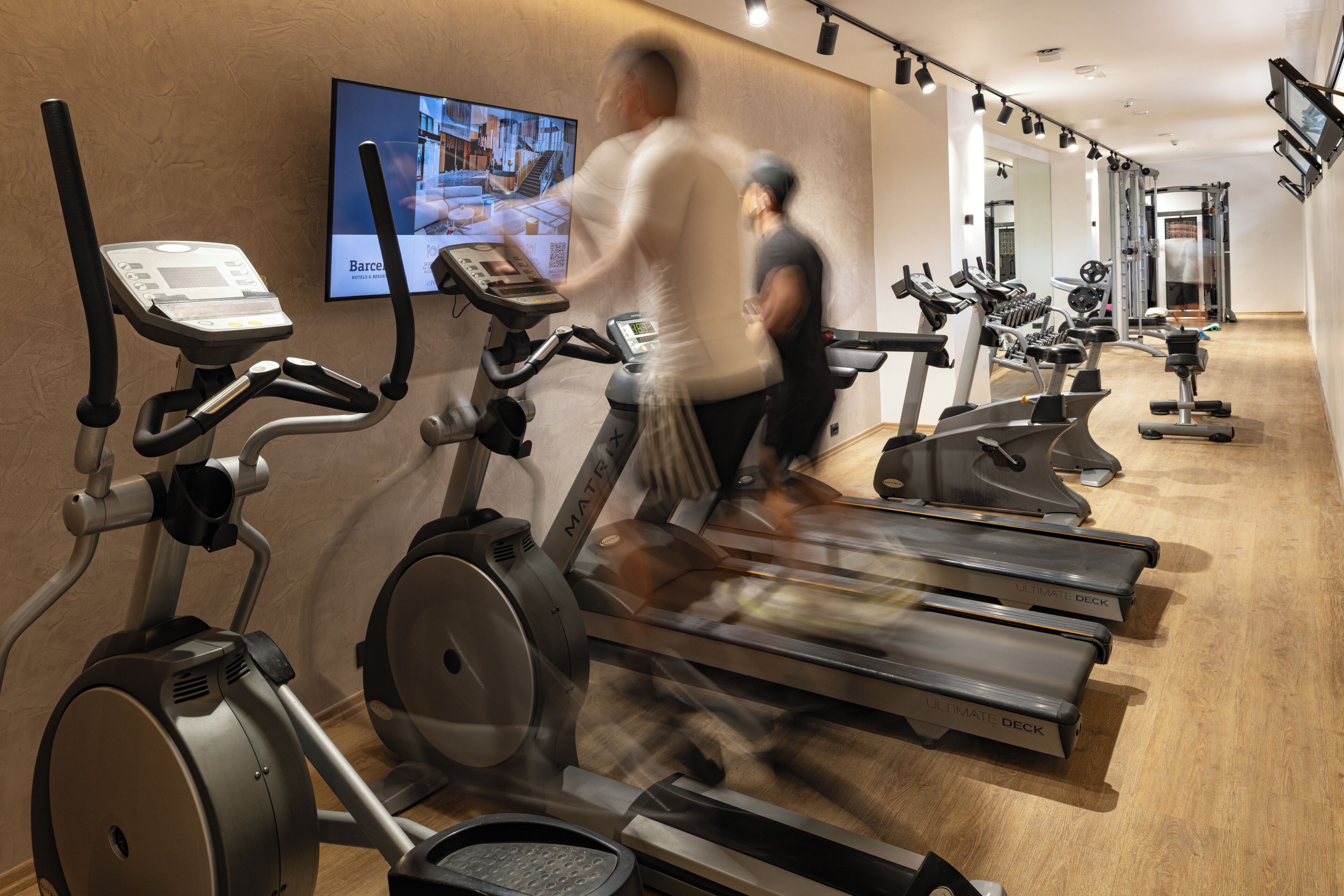 Un gimnasio con cintas de correr, bicicletas estáticas y una televisión que muestra un programa de ejercicios.