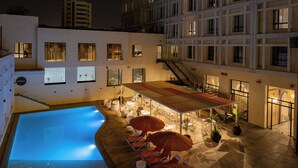 A rooftop pool area with lounge chairs and umbrellas, surrounded by buildings with illuminated windows. - Barceló Fès Medina (Fes)