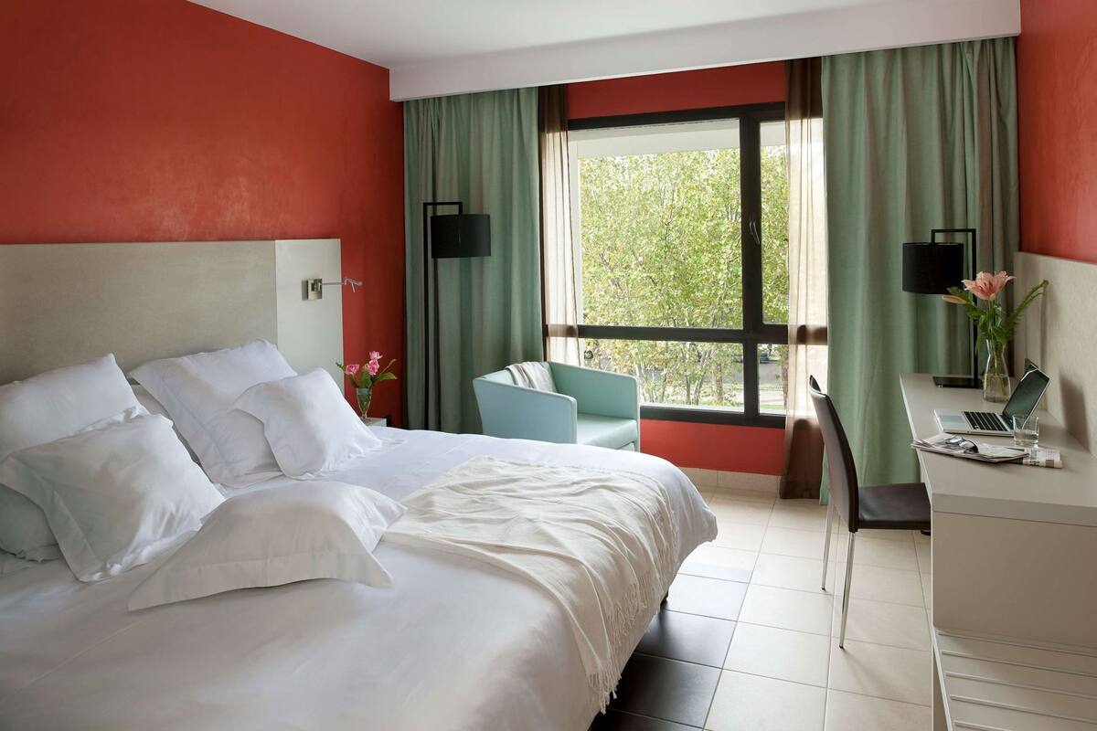 A hotel room with a bed, a desk, a chair, and a window with curtains.
