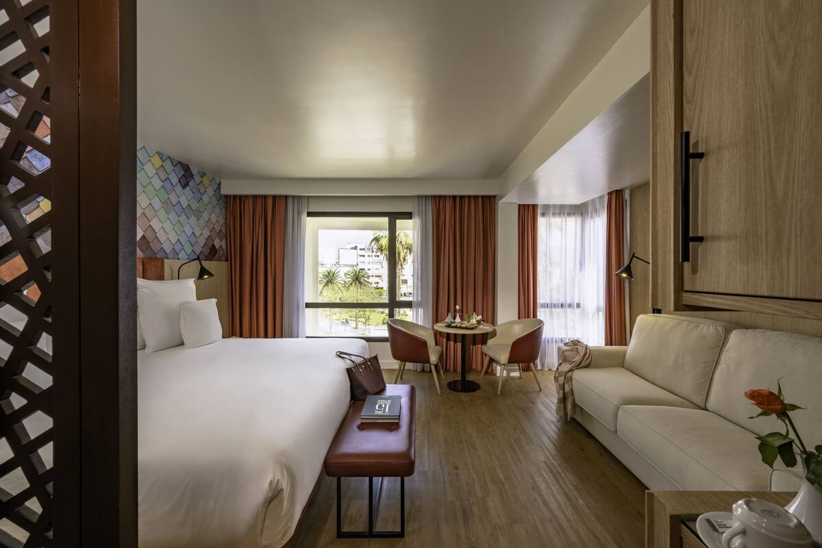 A hotel room with a bed, a sofa, a small table, and a window with curtains.