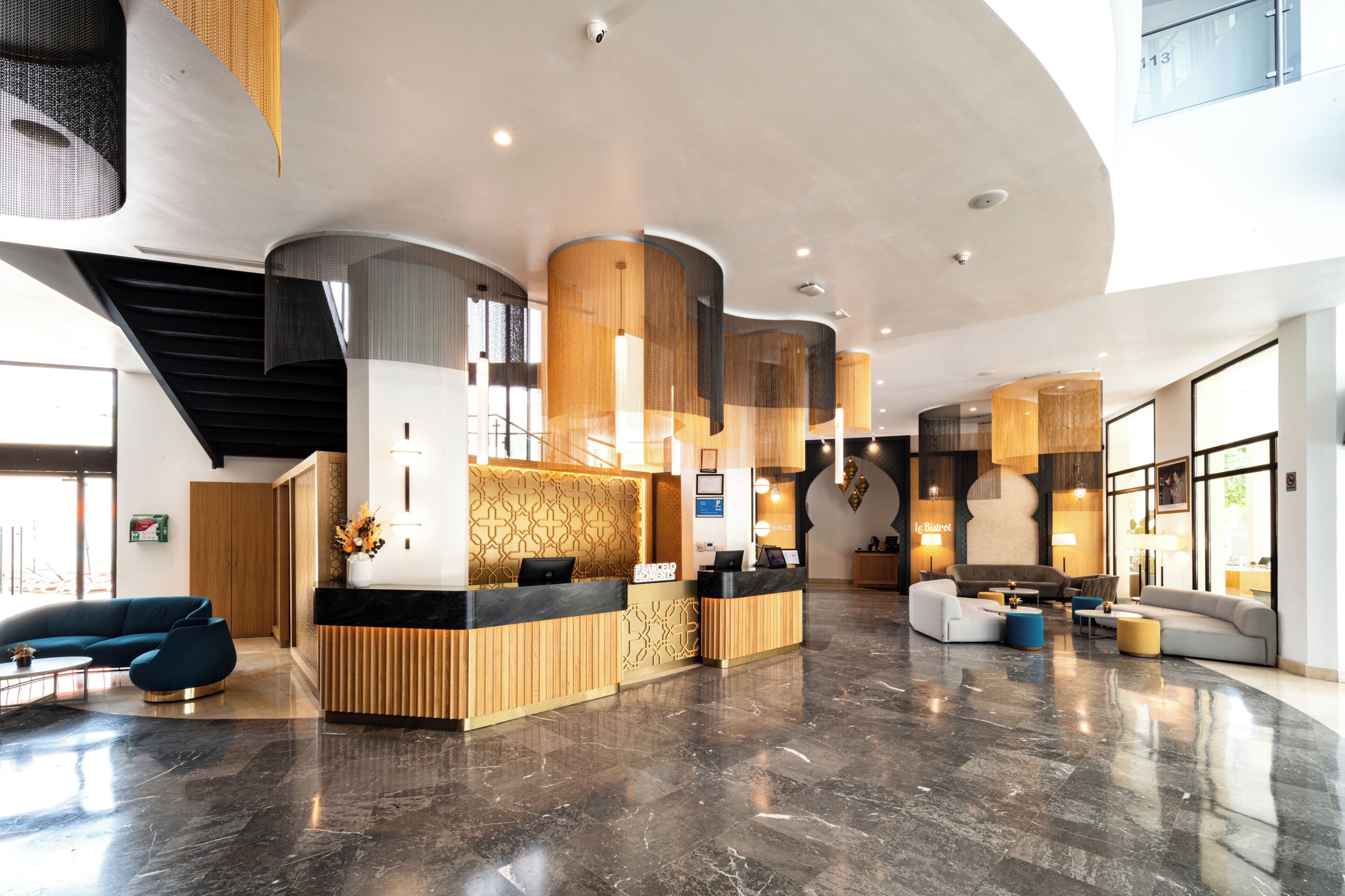 Un moderno vestíbulo de hotel con mostrador de recepción, zonas de estar y una escalera.