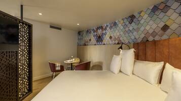 Quarto de hotel moderno com uma cama grande, uma mesinha redonda com duas cadeiras e uma parede decorativa com padrão geométrico.