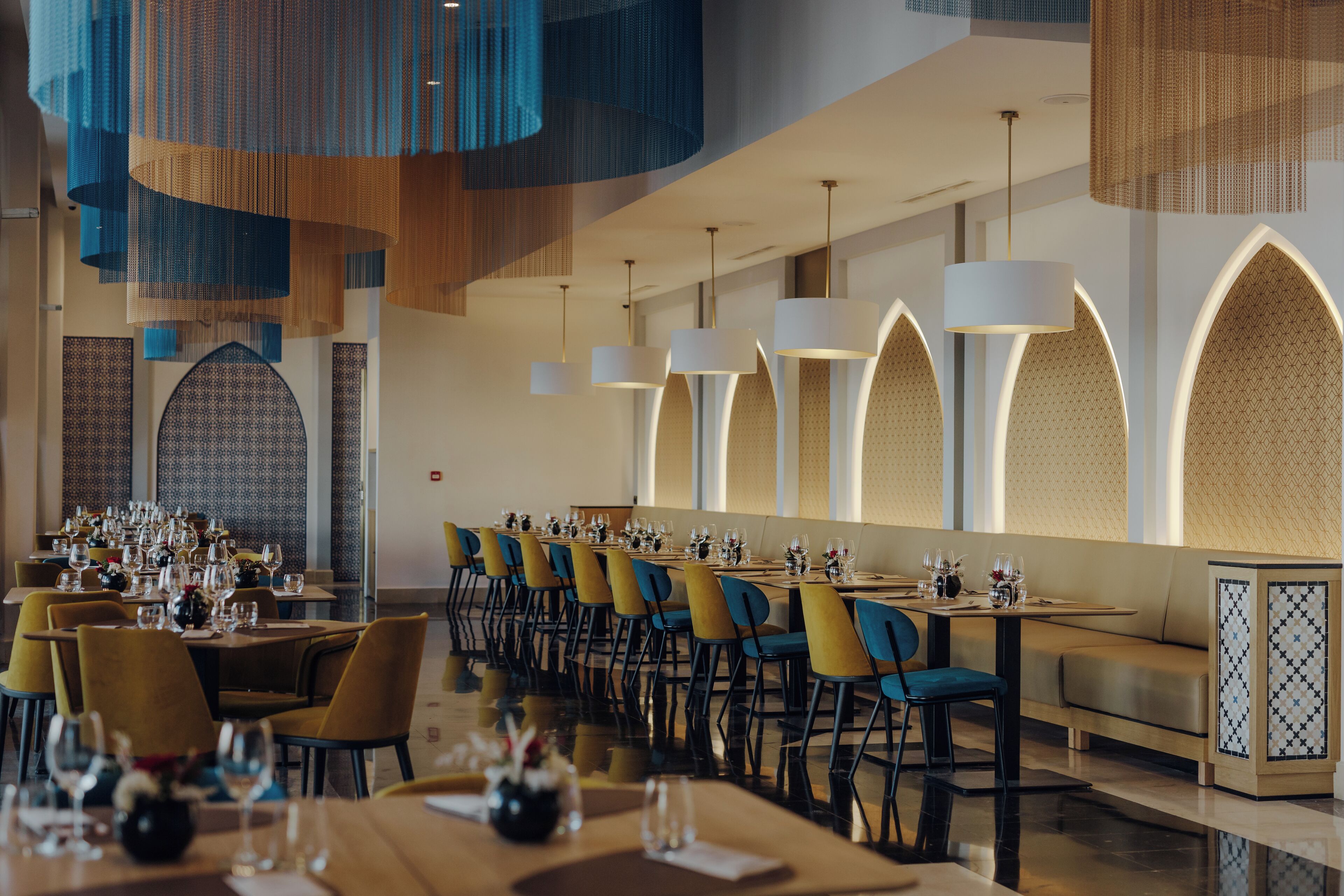 Un restaurante moderno con mesas largas, sillas azules e iluminación decorativa.
