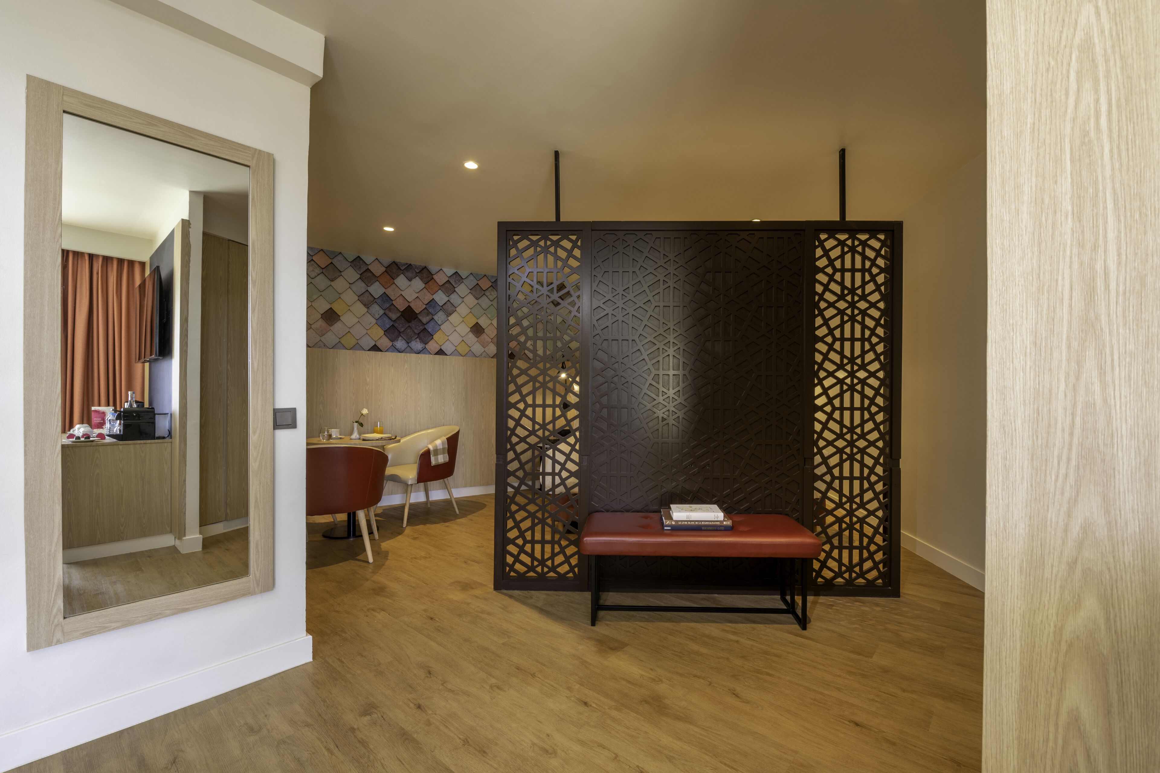 Een moderne hotelkamer met een houten vloer, een rode bank, een bureau met een stoel en een decoratief wandpaneel.