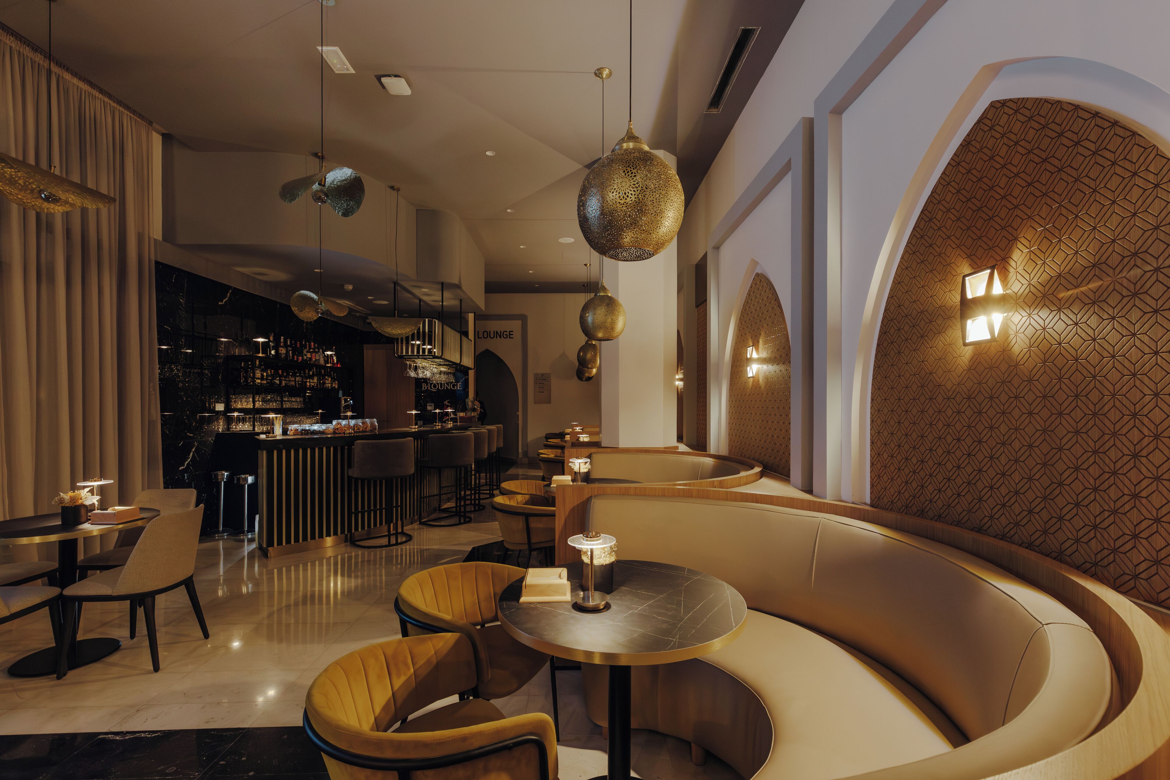 A modern lounge area with a curved seating arrangement, a bar in the background, and decorative lighting.