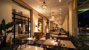 A modern indoor dining area with multiple tables and chairs, large windows, and decorative lighting. - Barceló Fès Medina (Fes)