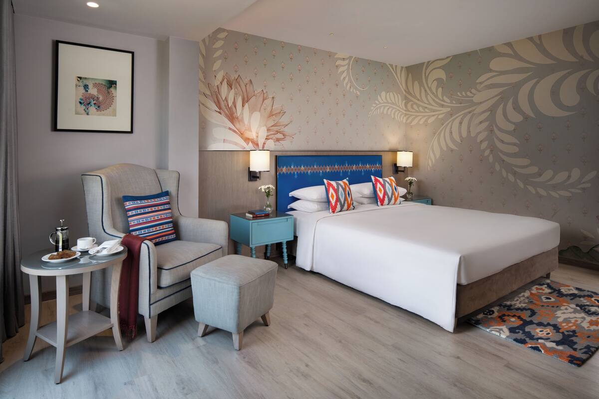 A hotel room with a large bed, a chair, a small table, and a nightstand.
