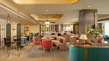 A modern hotel lobby with a seating area, a reception desk, and a dining space.