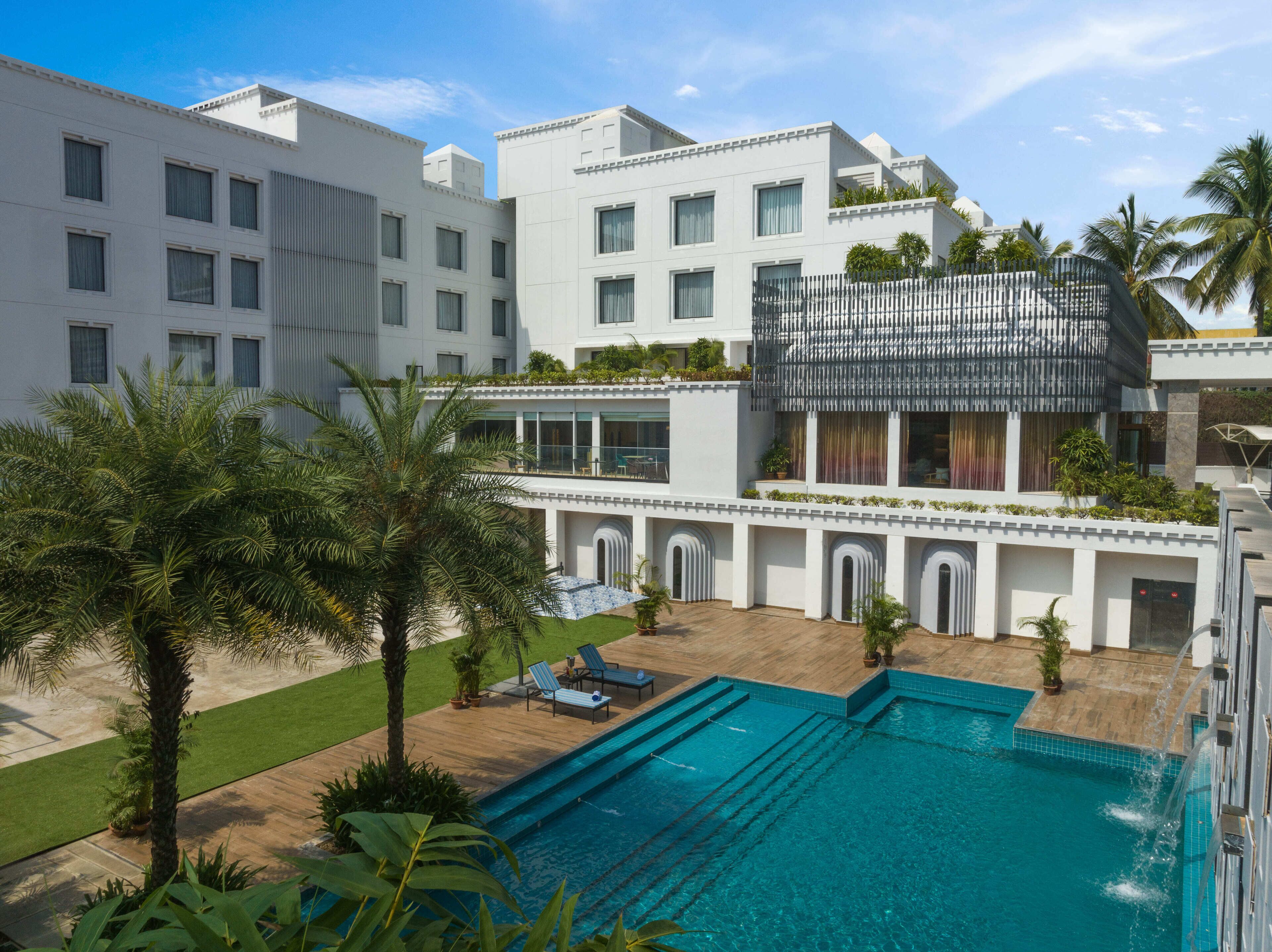 A modern hotel with a swimming pool, palm trees, and a covered outdoor area.