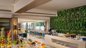 Un espace de restauration moderne dans un hôtel, avec un buffet, un mur à motifs verts et une vue sur l’extérieur.