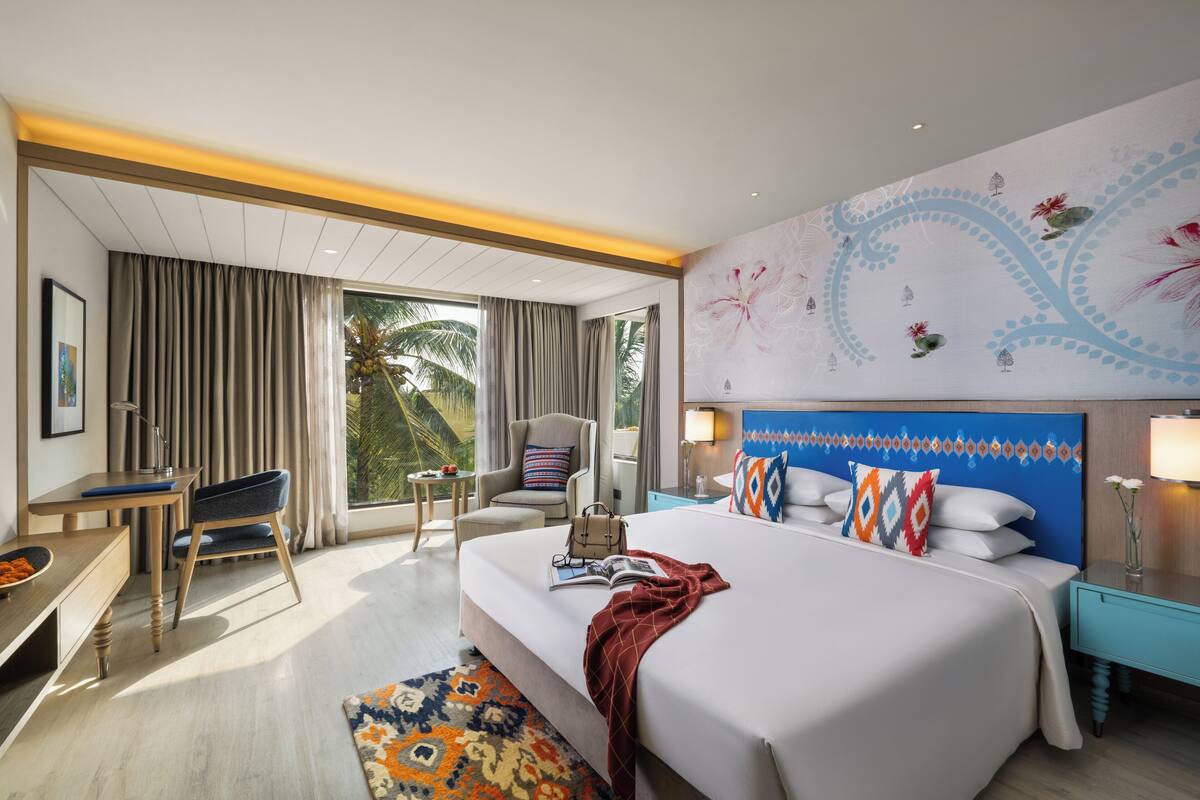A modern hotel room with a large bed, a desk, a chair, and a view of palm trees.