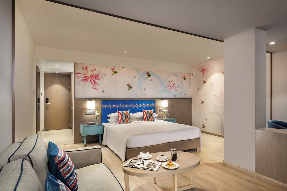 A hotel room with a bed, a sitting area with a table, and a nightstand with a lamp.