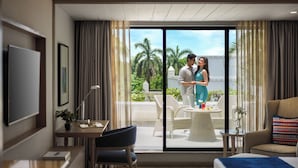 Une chambre d’hôtel avec un lit, un bureau, une chaise, une petite table et une grande fenêtre avec des rideaux.