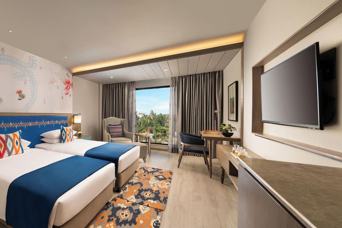 A hotel room with two beds, a desk, a TV, and a view of the outdoors.