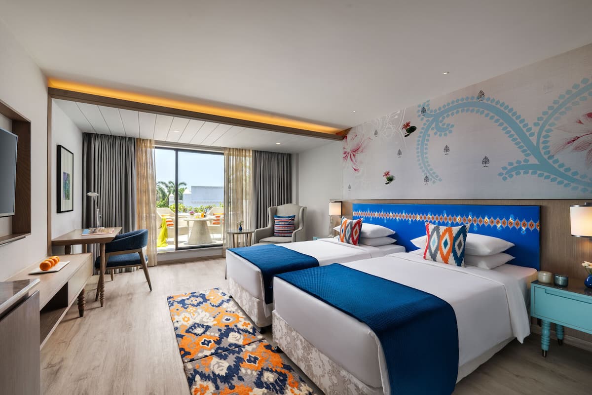 A hotel room with two beds, a desk, a chair, a TV, and a balcony with a view.