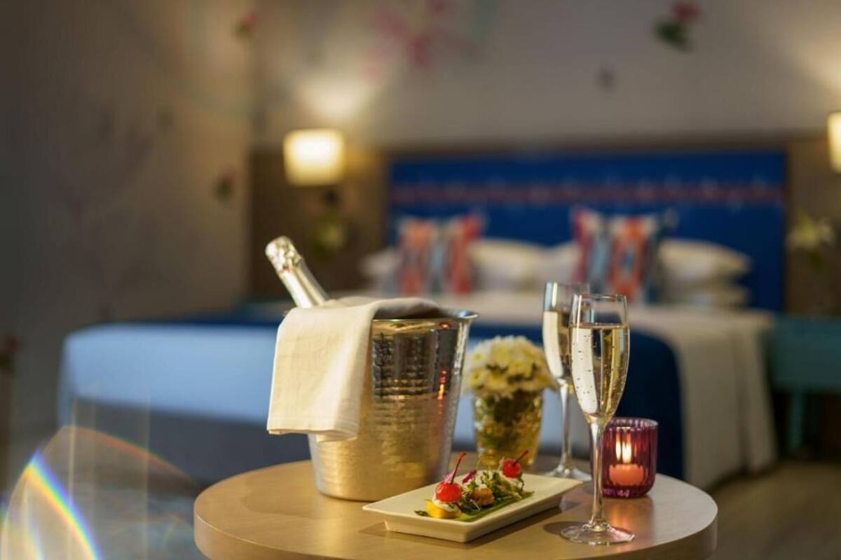 A hotel room with a bed, a minibar, a small table with a drink and a glass, and a decorative wall.