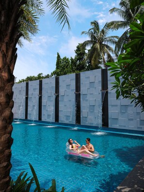 A swimming pool with clear blue water, surrounded by palm trees and a stone wall.