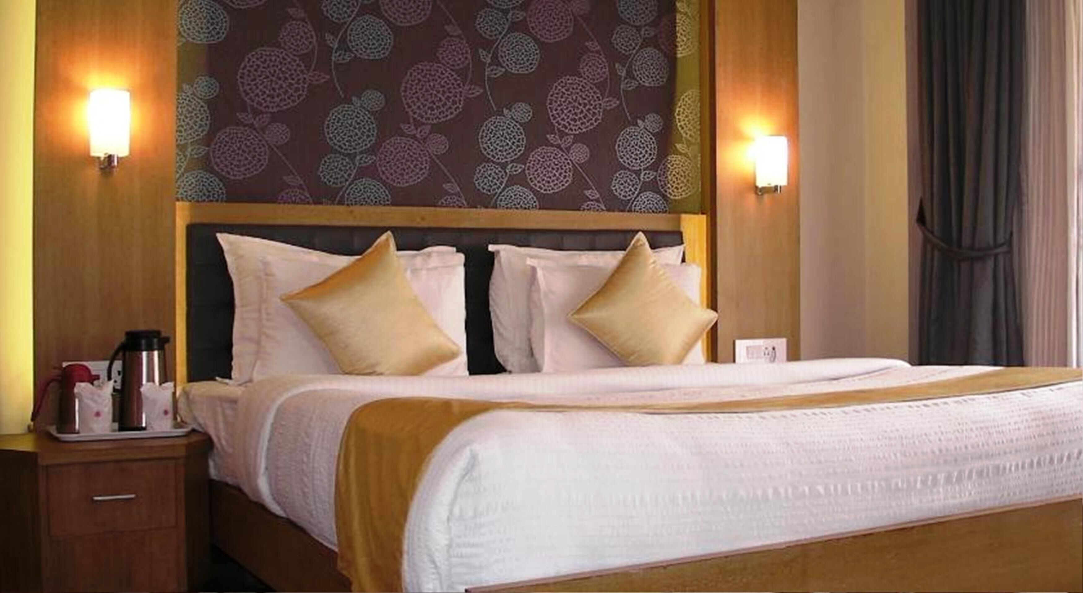 A hotel room with a large bed, two bedside tables, and a patterned wallpaper.