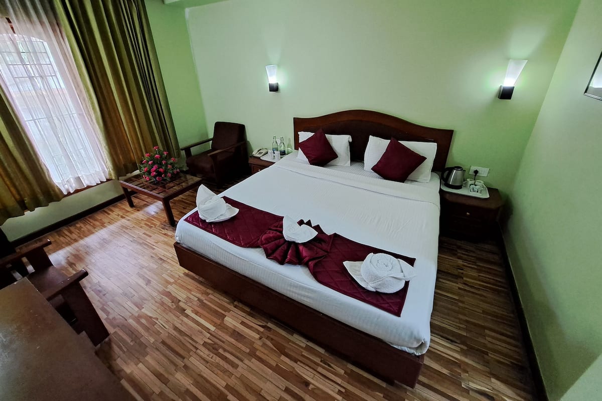 A neatly made bed with white and maroon bedding, a wooden headboard, and a bedside table with a lamp and a phone.
