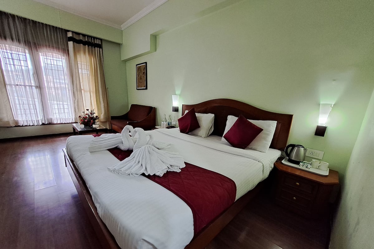 A hotel room with a large bed, a wooden nightstand, a bedside table, and a window with curtains.