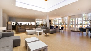 A spacious hotel lobby with a high ceiling, large windows, and a central seating area with sofas and tables. - Apartamentos Jutlandia (Calvia)