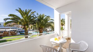 A balcony with white chairs, a small table, and a view of a pool and palm trees. - Apartamentos Jutlandia (Calvia)
