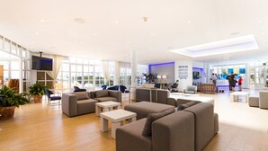 A spacious lobby with modern furniture, large windows, and a flat-screen TV. - Apartamentos Jutlandia (Calvia)