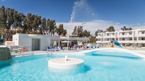 A swimming pool with a water fountain, lounge chairs, and a water slide. - Apartamentos Jutlandia (Calvia)