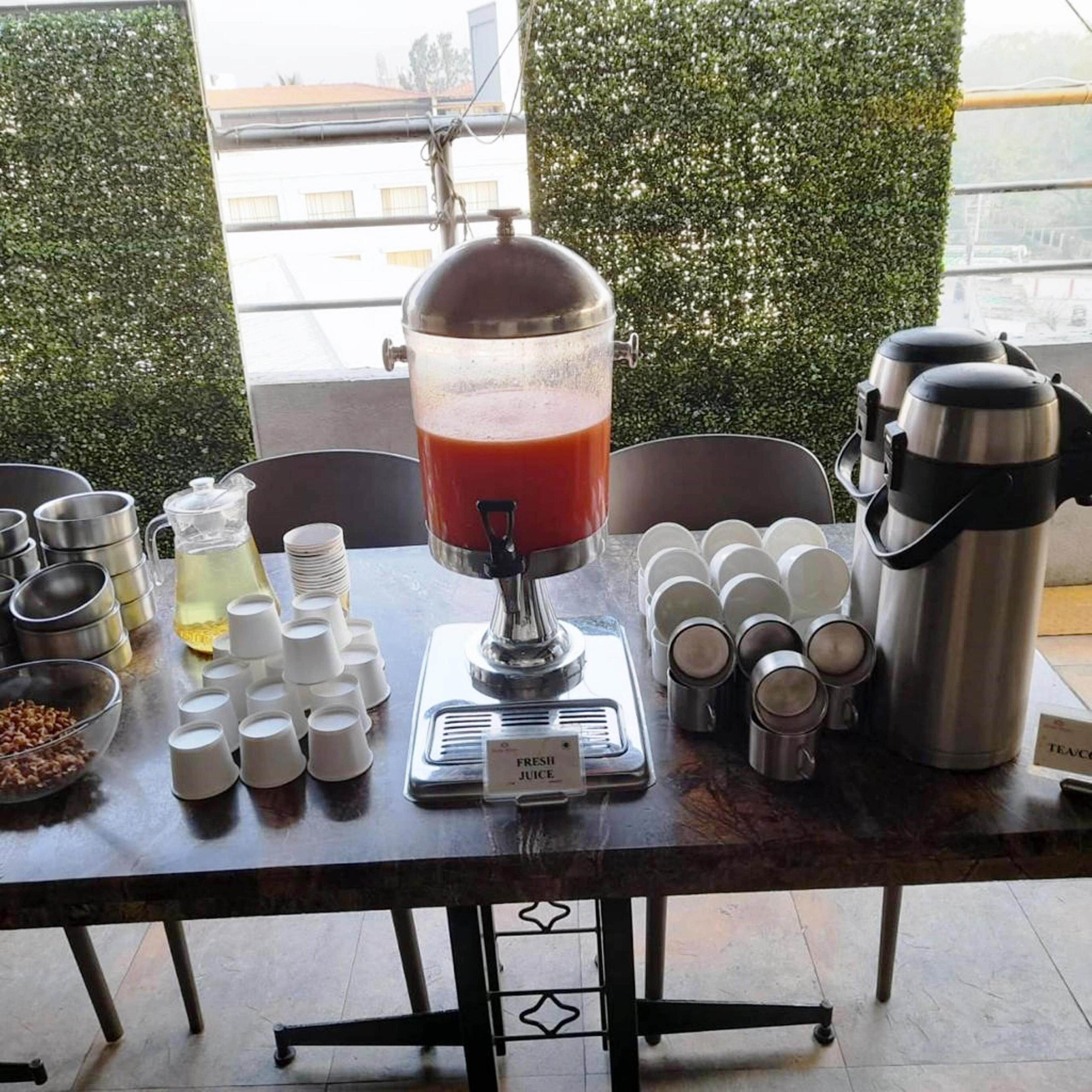 A juice bar setup with a large dispenser, multiple cups, and a sign indicating 'Fresh Juice'.