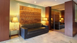 Un hall d’entrée moderne avec un canapé en cuir foncé, deux tables d’appoint avec des lampes et un mur à motifs.