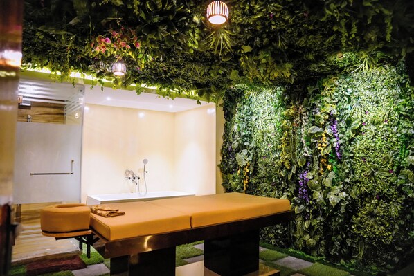 A spa room with a massage table, a bathtub, and a wall covered in greenery.