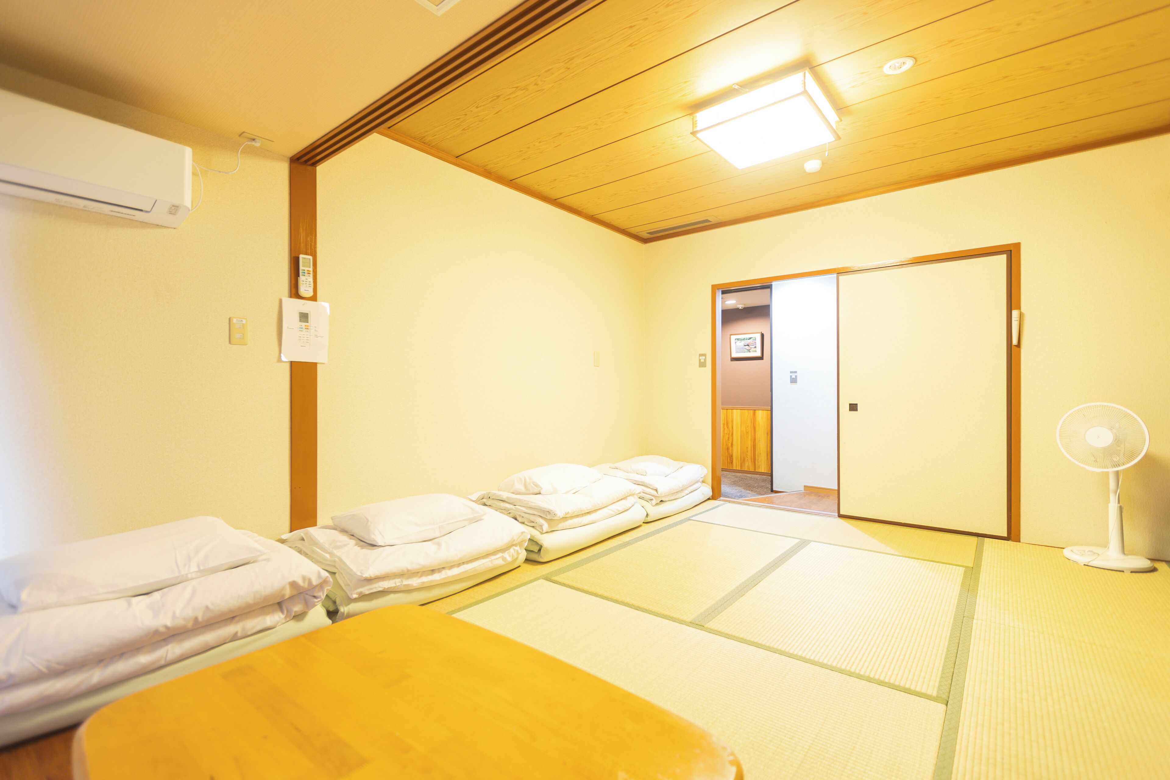 A room with tatami mats, a wooden ceiling, and a bed with white bedding.