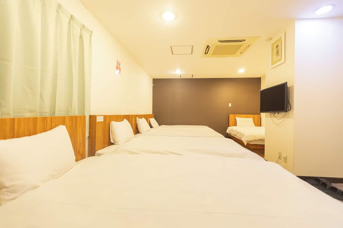 Habitación de hotel con dos camas individuales, un cabecero de madera, un televisor de pantalla plana en la pared y una ventana con cortinas.