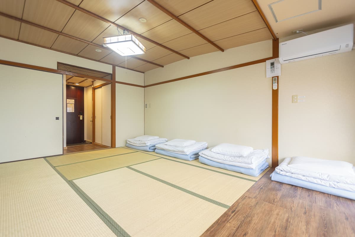 Una habitación japonesa tradicional con suelo de tatami, techo de madera y una puerta corredera que da a otra estancia.