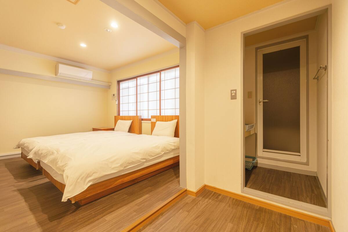 Un dormitorio con una cama de madera, una ventana con persianas, un equipo de aire acondicionado y una puerta que da a un armario.