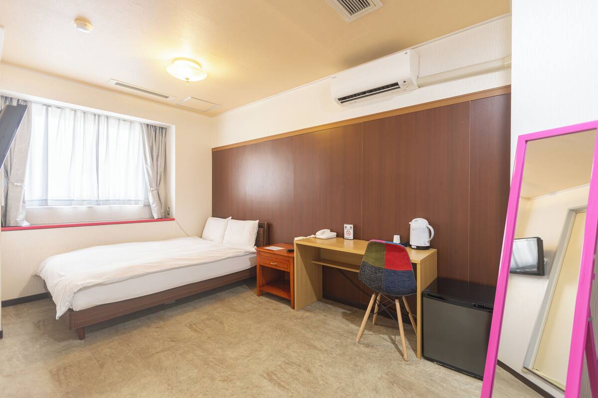 Una habitación de hotel con cama, escritorio, silla y un pequeño refrigerador.