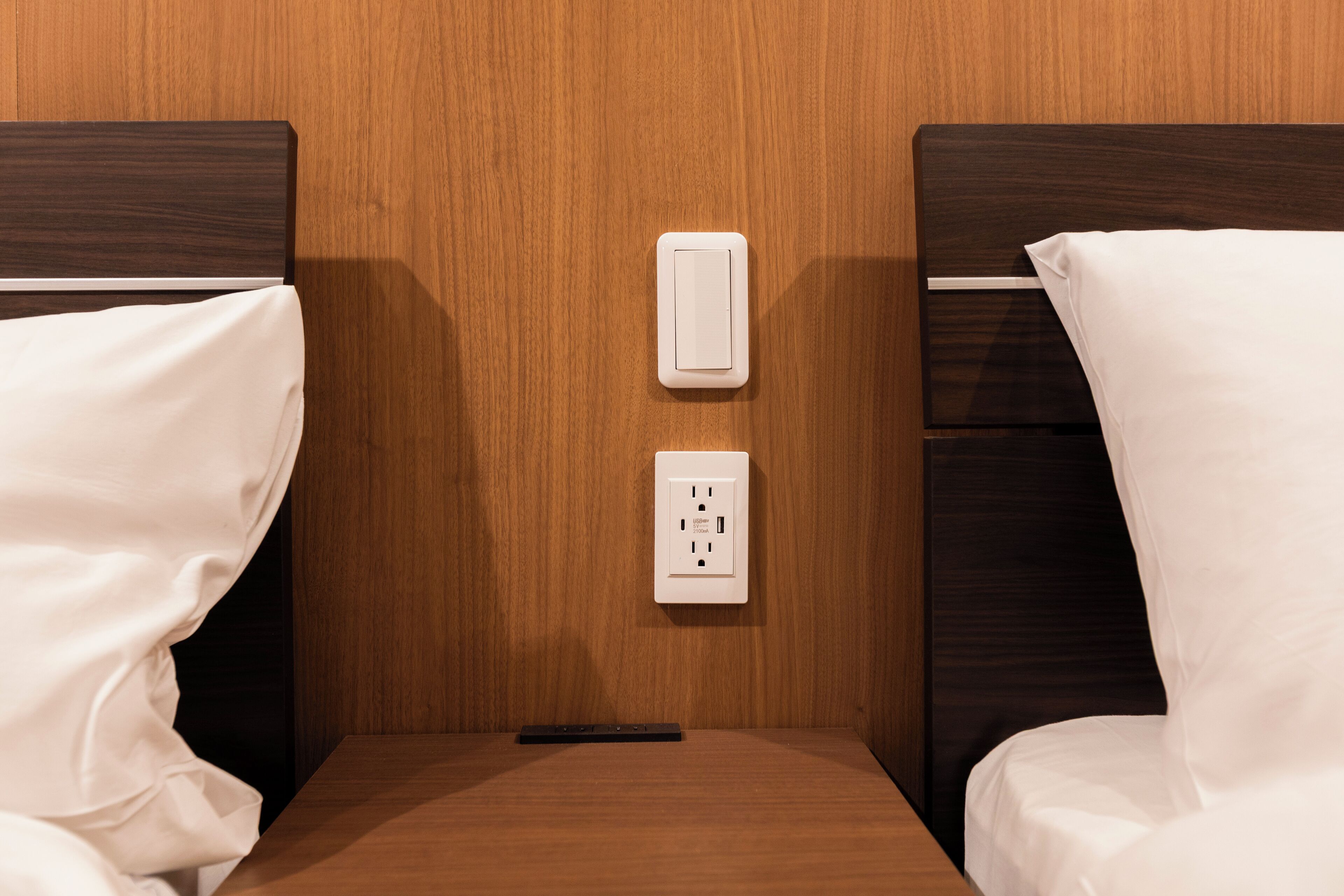 Ein Hotelzimmer mit zwei hölzernen Kopfteilen, einer weißen Steckdose und einer Fernbedienung auf dem Nachttisch.