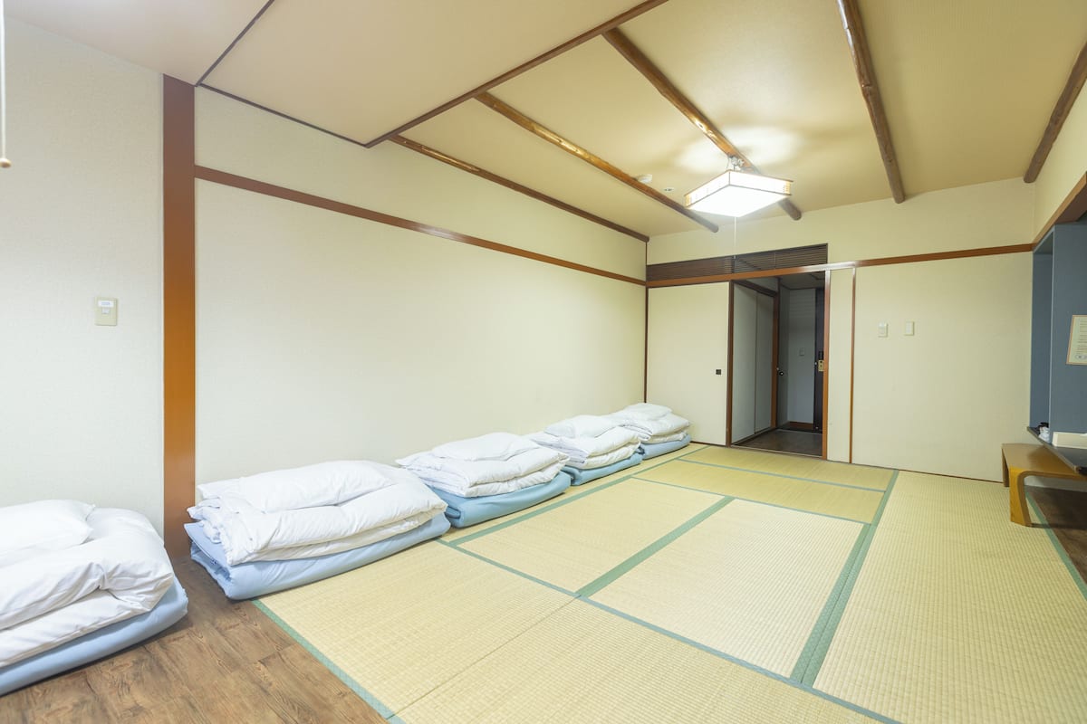 Una habitación con tatamis, suelo de madera y una cama con ropa de cama blanca.