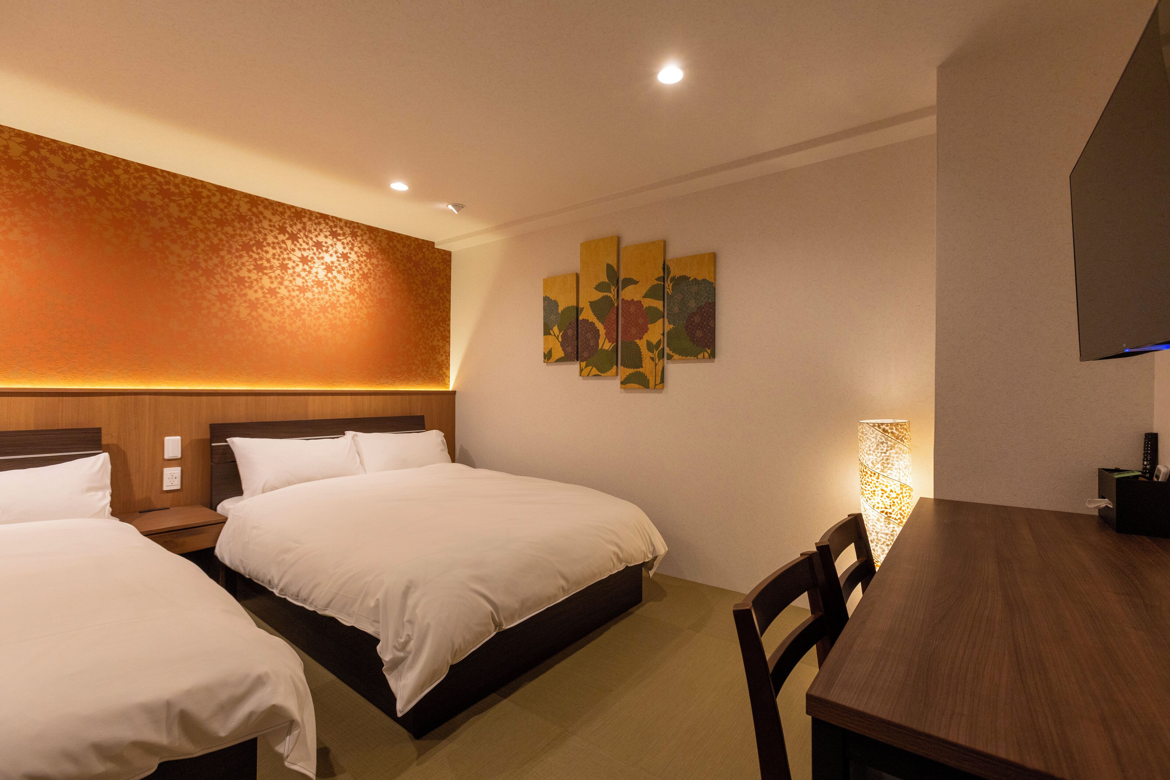 A hotel room with two beds, a wooden headboard, a dining table, and a wall-mounted artwork.