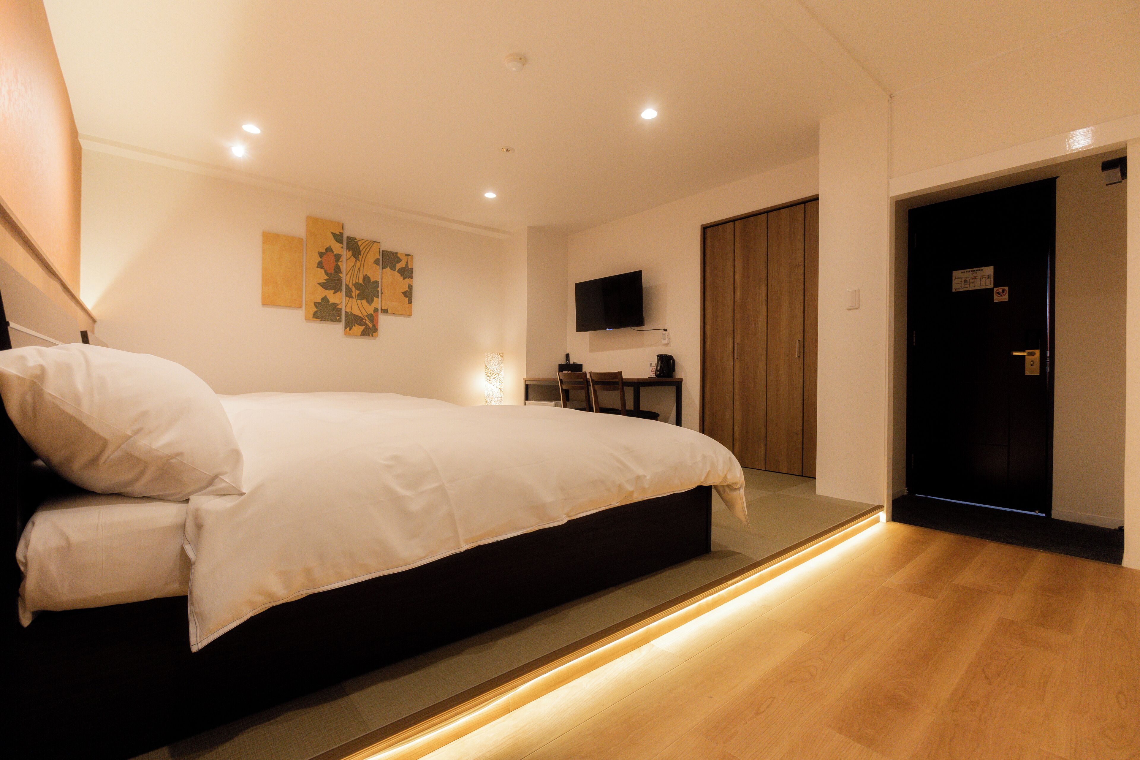 Un dormitorio moderno con una cama grande, un televisor de pantalla plana montado en la pared y un armario de madera.
