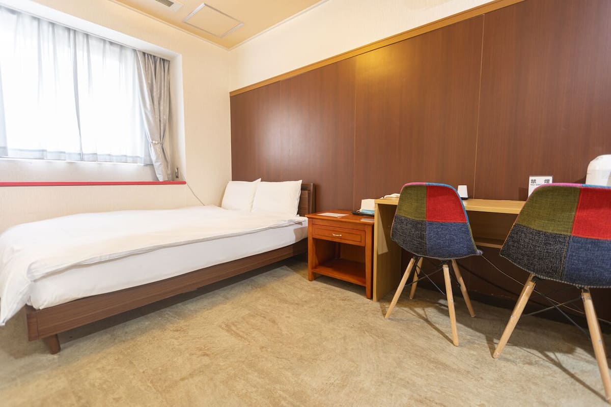 Une chambre d’hôtel avec un lit, un bureau, une chaise et une fenêtre avec des rideaux.
